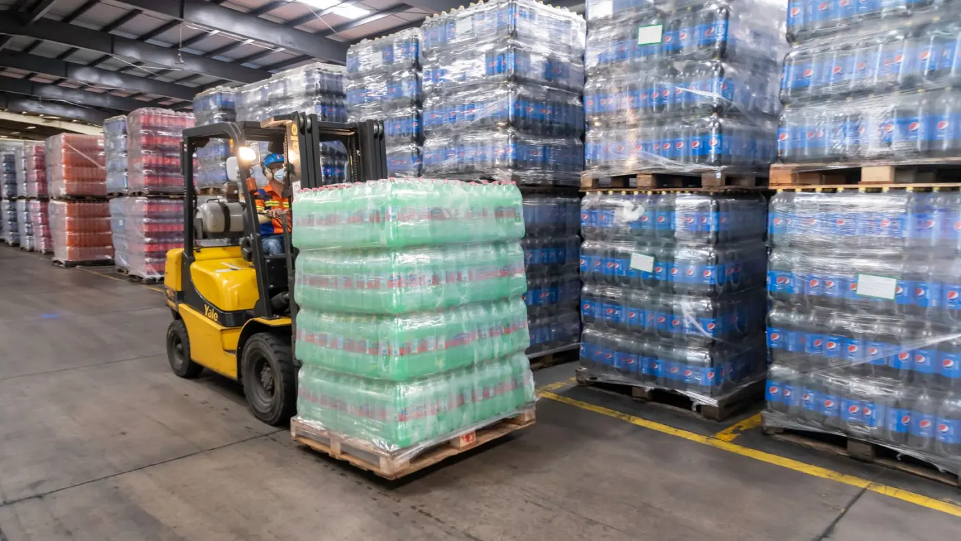 A forklift moving stacked pallets in a distribution warehouse