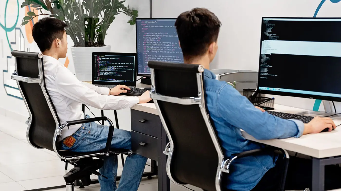 Two engineers working through code on adjacent monitors